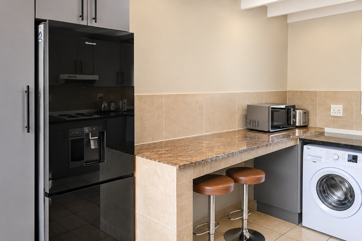 Modern kitchen featuring granite countertops, tiled backsplash, built-in cabinetry, integrated washing machine, and a breakfast bar area.