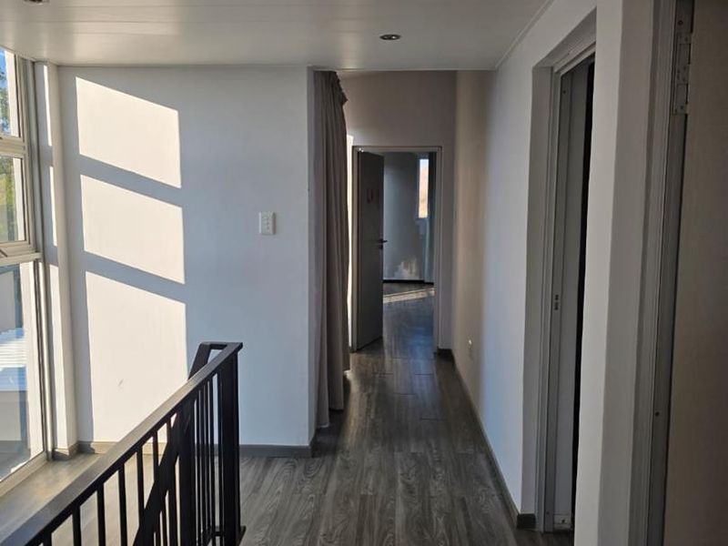 A bright, modern hallway featuring laminate timber-look flooring, recessed downlighting, and a sleek metal balustrade overlooking the lower level.
