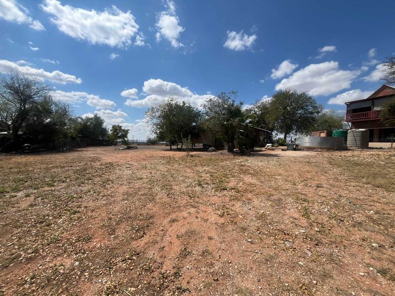 A large, undeveloped outdoor garden area featuring mature trees and external water storage tanks on the property grounds.