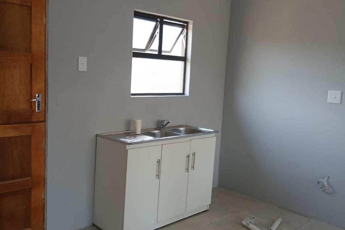 A compact, empty kitchen area featuring tiled flooring, a stainless steel sink unit, and a timber door, presenting a clean, neutral canvas.