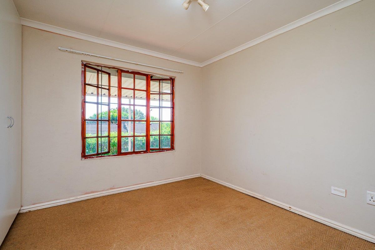 A vacant bedroom featuring neutral walls, fitted carpeting, and a wooden-framed window with security bars.