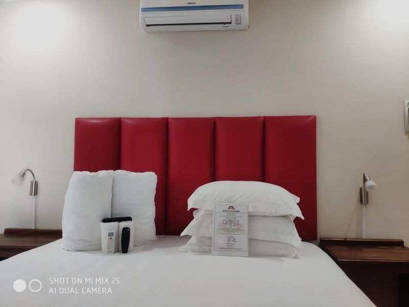 A bedroom featuring a red upholstered headboard, wall-mounted reading lights, and a split-system air conditioning unit.