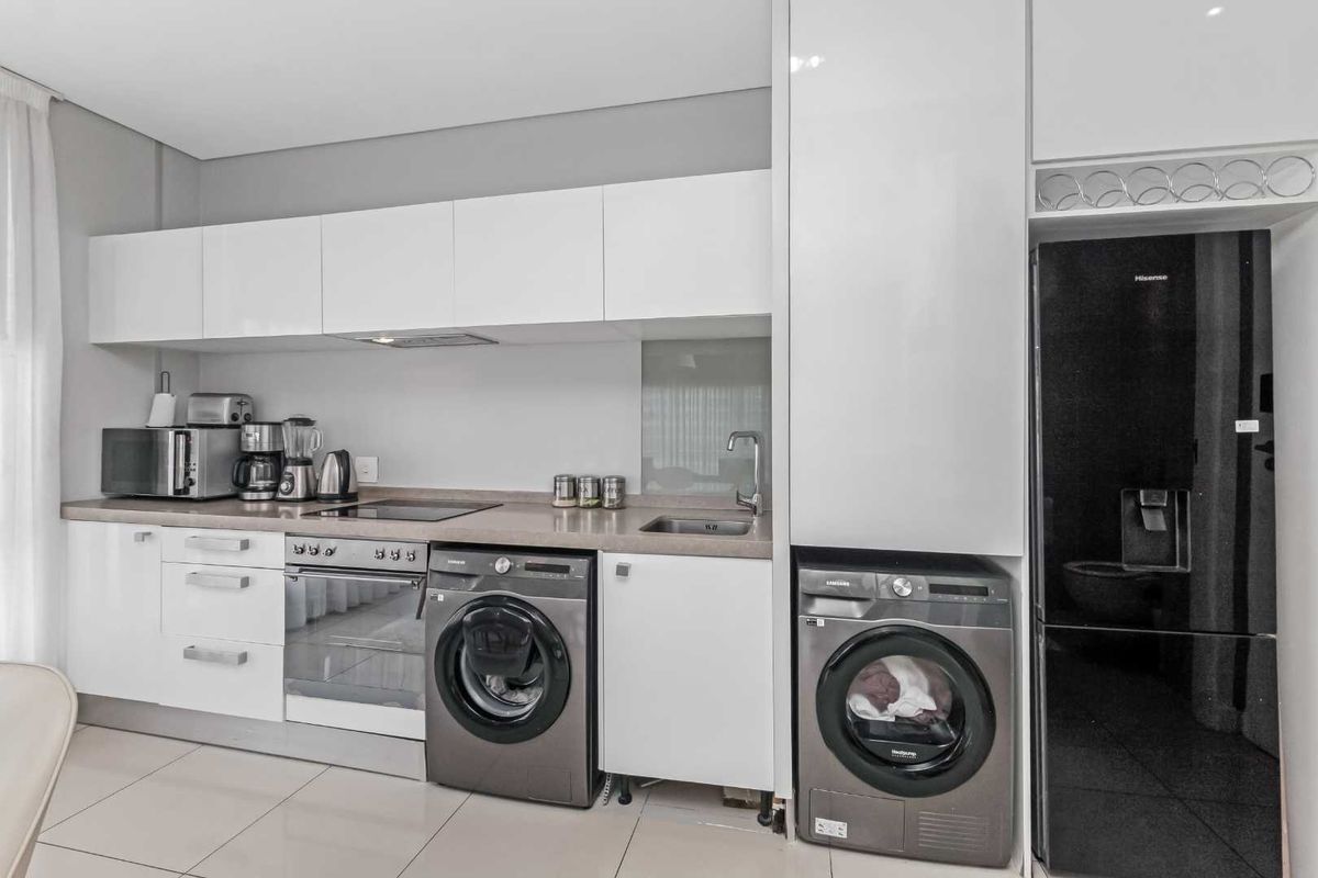 Modern kitchen featuring sleek white cabinetry, integrated oven and hob, stainless steel sink, and dedicated spaces for laundry appliances.