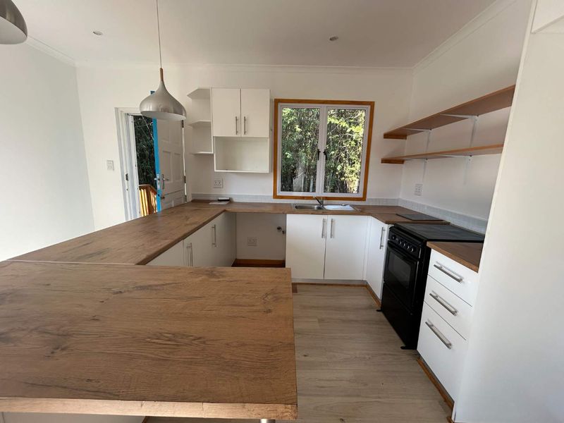 A bright, modern kitchen featuring white cabinetry, warm wooden countertops, open shelving, and a freestanding oven, offering a clean and functional workspace.