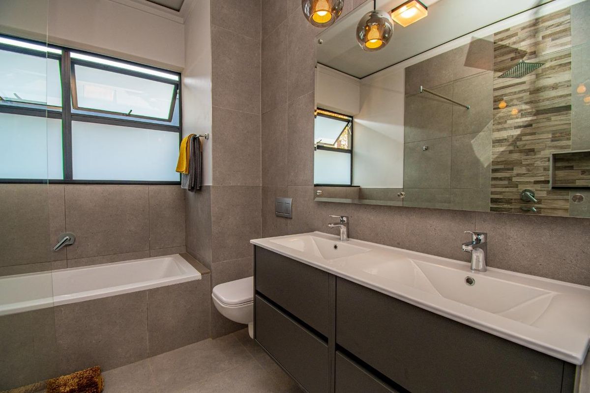 Modern bathroom featuring a double vanity with integrated sinks, a wall-mounted toilet, and a tiled bathtub with a glass shower screen.