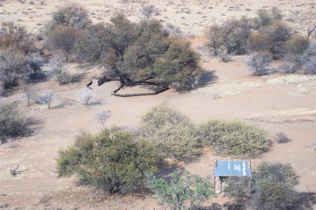 Aerial view of a rural farm property featuring natural landscape, scattered trees, and small rustic outbuildings with corrugated metal roofing.