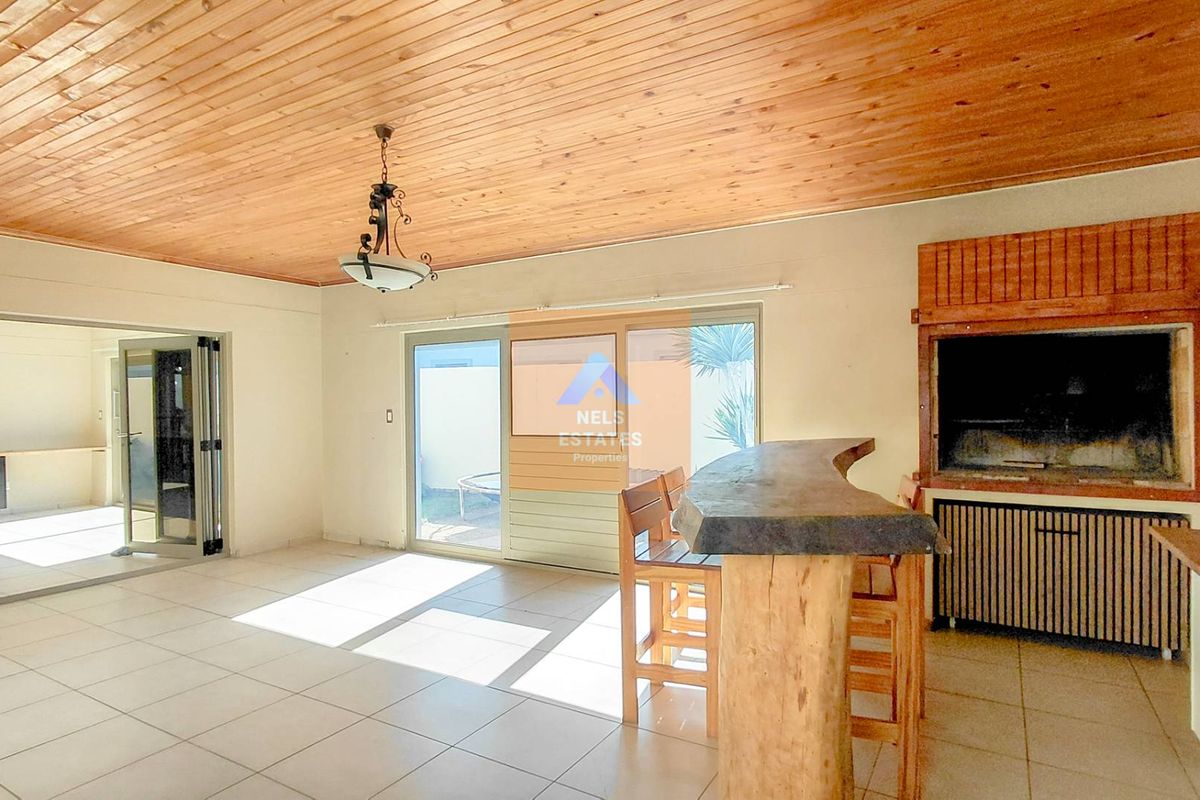 Spacious entertainment area featuring a built-in braai, wooden ceiling, tiled flooring, and sliding doors leading to an outdoor space.