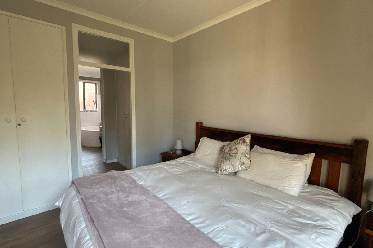 A well-lit bedroom featuring neutral walls, laminate flooring, and a built-in wardrobe, with an adjoining view into the bathroom area.