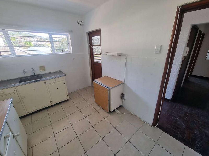 A dated, empty kitchen featuring tiled flooring, a stainless steel sink, and basic cabinetry, offering a blank canvas for renovation.