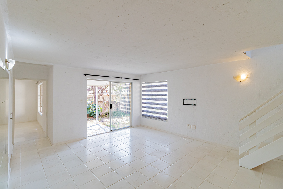 An empty, open-plan living area featuring white tiled flooring, a staircase, and a sliding glass door providing access to the rear garden.