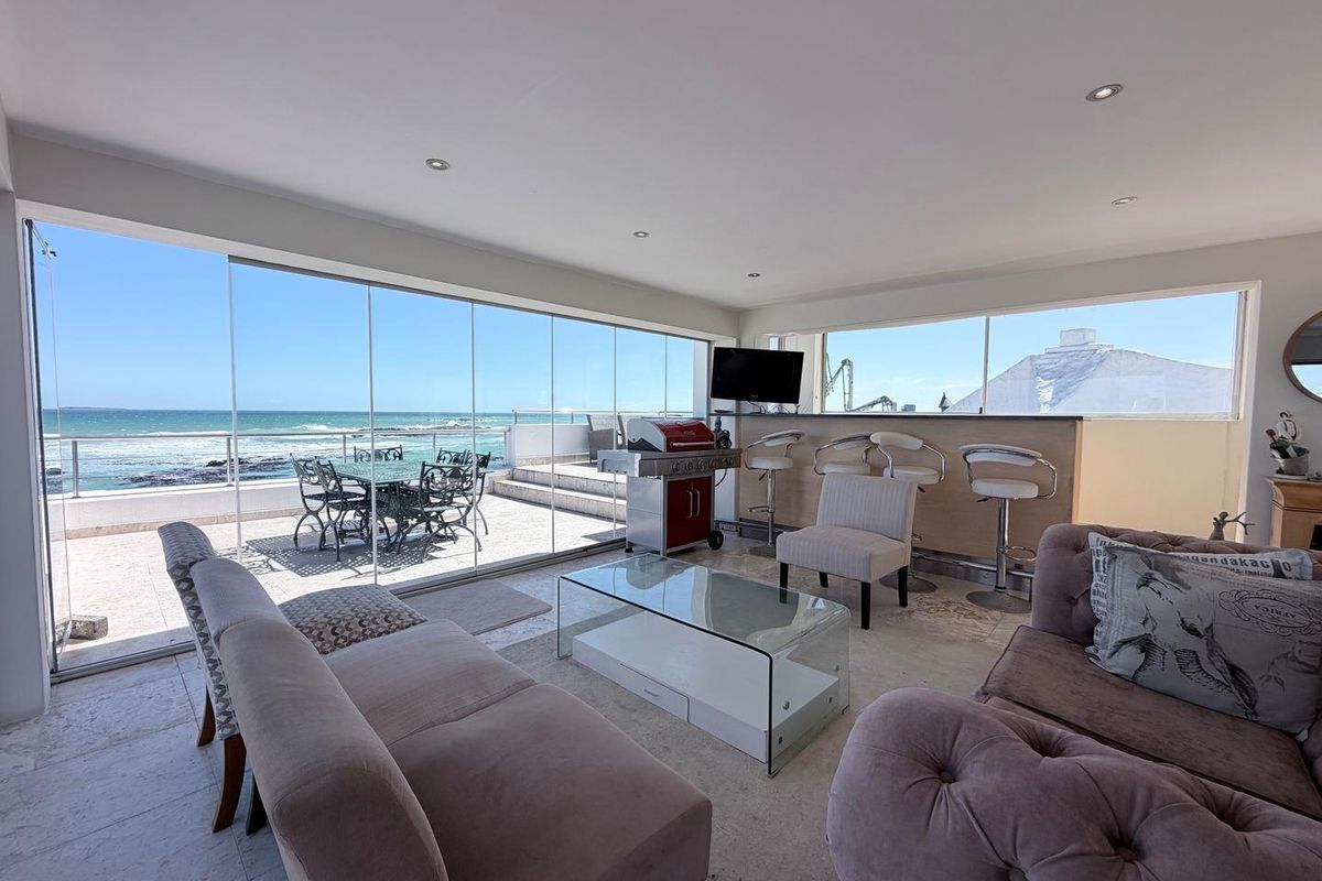 Spacious living area featuring large glass sliding doors that open onto a patio with panoramic ocean views and a built-in bar counter.