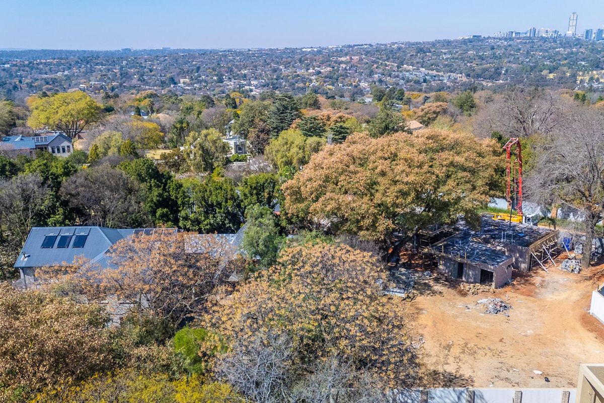 Aerial view of a residential property under construction, featuring a concrete slab foundation, mature trees, and surrounding suburban landscape.