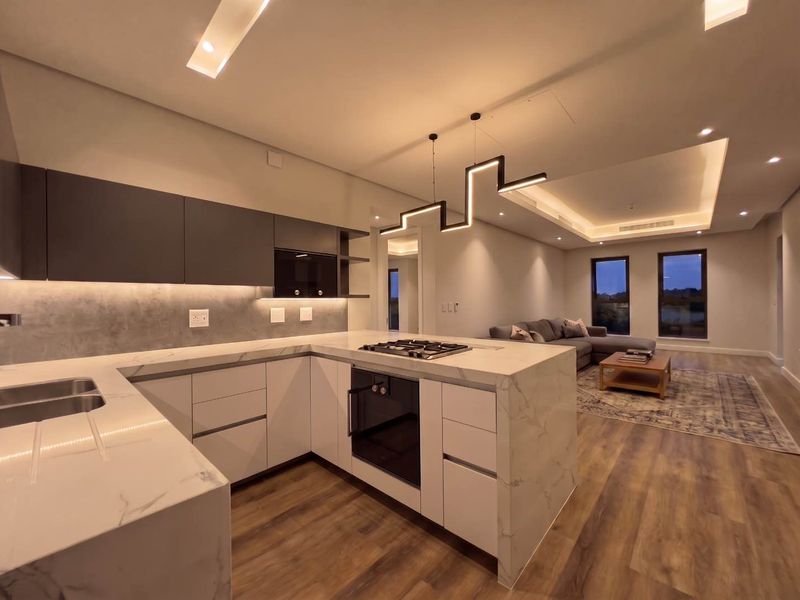 Modern open-plan kitchen and living area featuring high-end marble-look countertops, integrated appliances, sleek cabinetry, and sophisticated recessed and pendant lighting throughout.