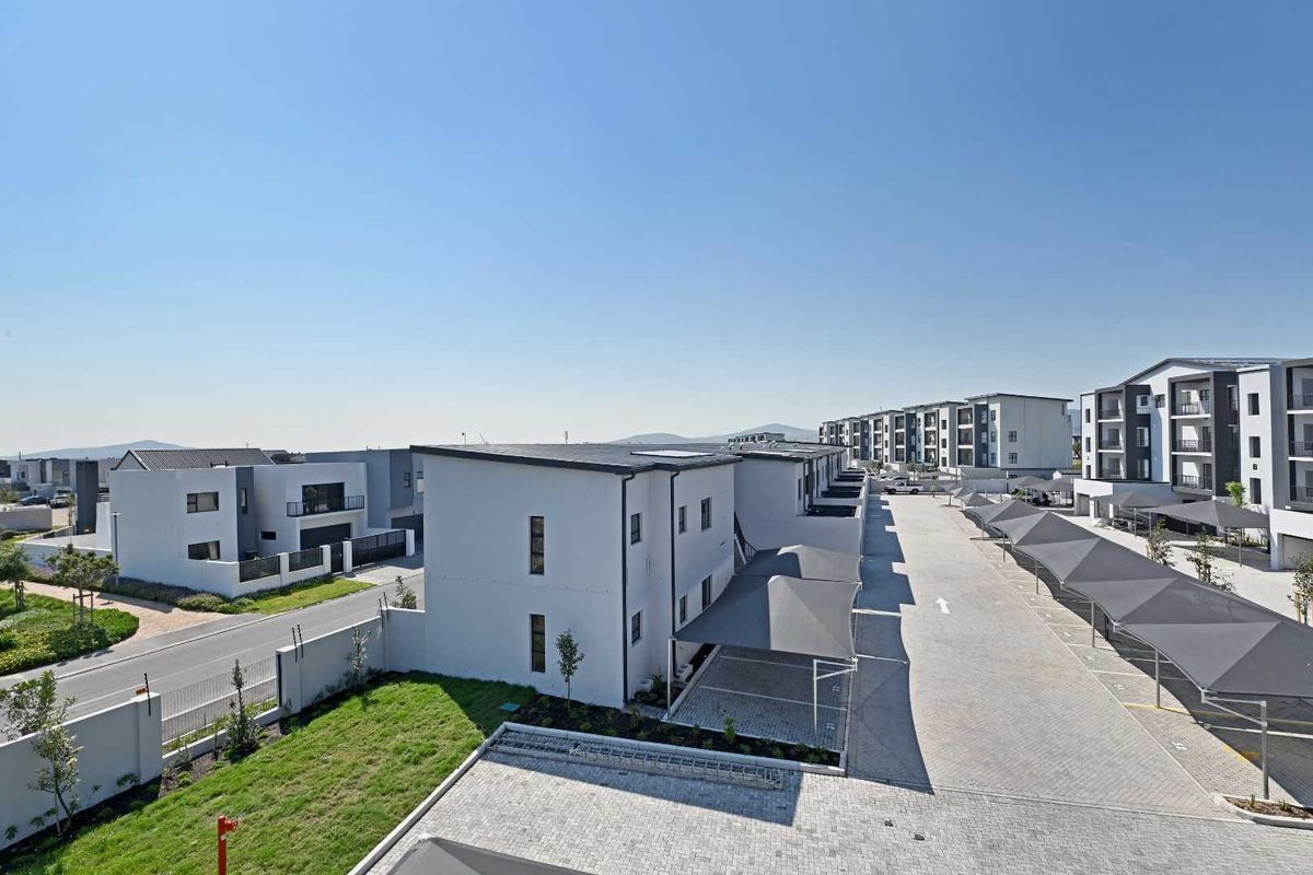 Aerial view of a modern apartment complex featuring paved driveways, covered parking bays, and well-maintained landscaped grounds.