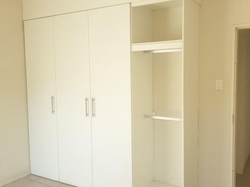 A clean, empty bedroom featuring neutral walls, tiled flooring, and ample built-in cupboard storage space.