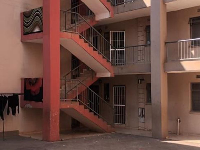Exterior view of a multi-story townhouse complex featuring an open-air concrete staircase, metal security gates, and a paved communal courtyard area.