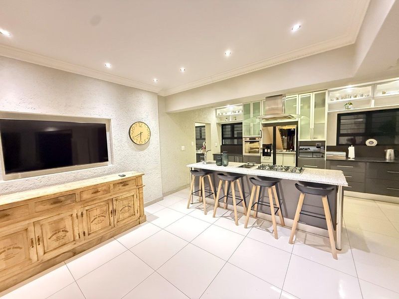 Modern open-plan living and kitchen area featuring sleek cabinetry, a central island with gas cooktop, granite countertops, and bright tiled flooring.