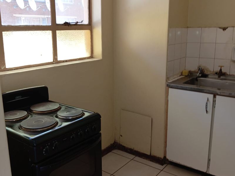 A compact kitchen featuring tiled flooring, a stainless steel sink with tiled splashback, and a freestanding electric stove.