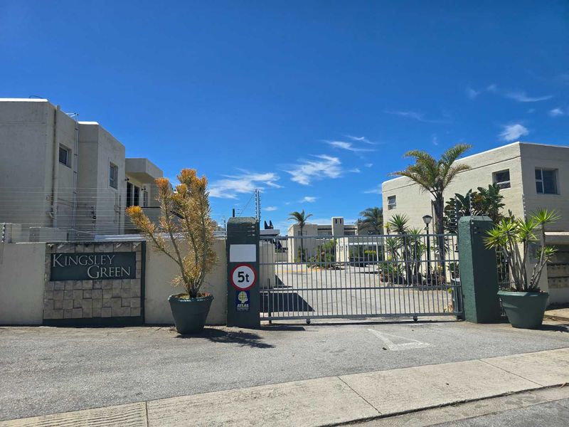 Front entrance view of Kingsley Green apartment complex featuring a secure gated access point, paved driveway, and perimeter electric fencing.