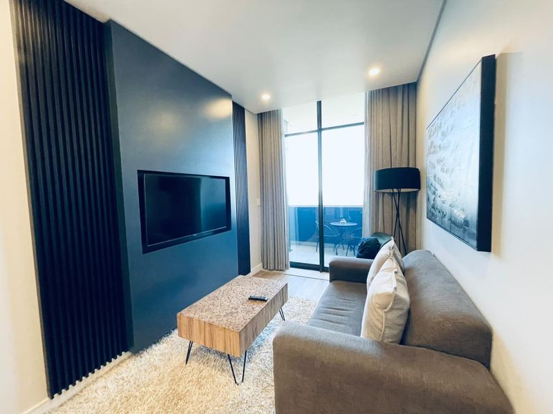 Modern living room featuring a dark blue accent wall with integrated television space, recessed lighting, and direct access to a private balcony.