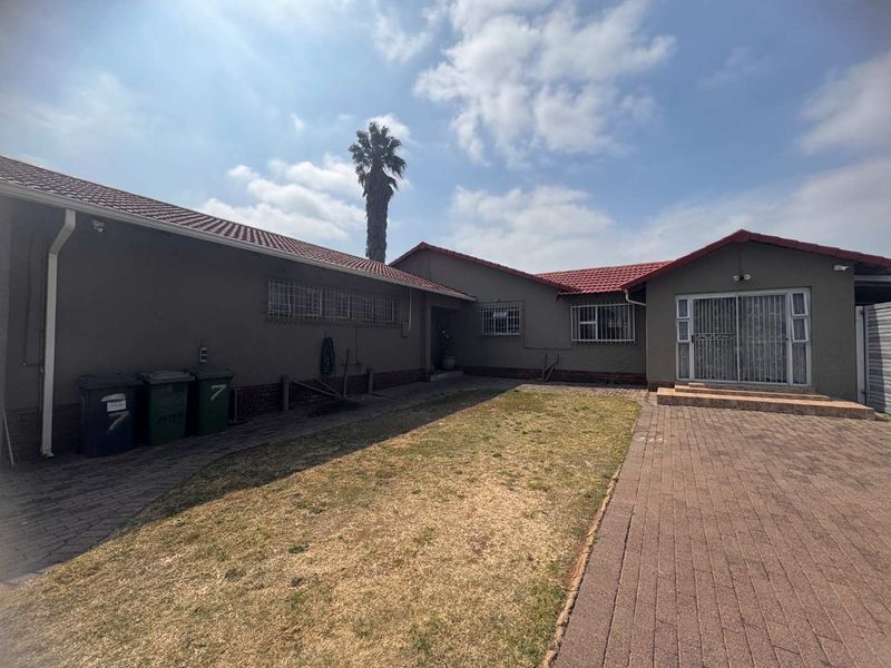 Rear view of the property featuring a paved courtyard, lawn area, tiled roof, and sliding door access with security bars.