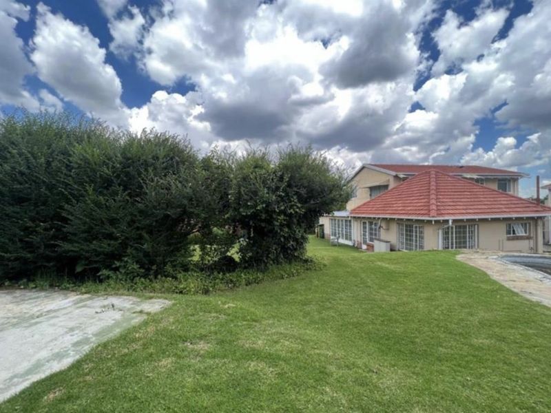 Rear view of the property featuring a spacious lawn, a swimming pool, and a tiled roof structure.