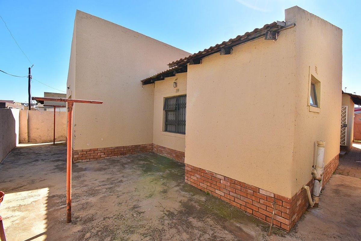 Rear exterior view of the property featuring a paved courtyard area, brick base detailing, and security bars on the window.