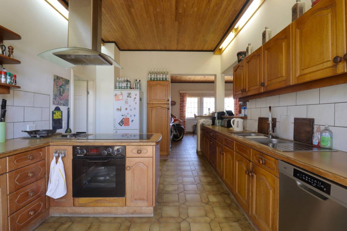 A functional kitchen featuring wooden cabinetry, built-in oven, hob, extractor fan, and tiled flooring with a wooden ceiling finish.
