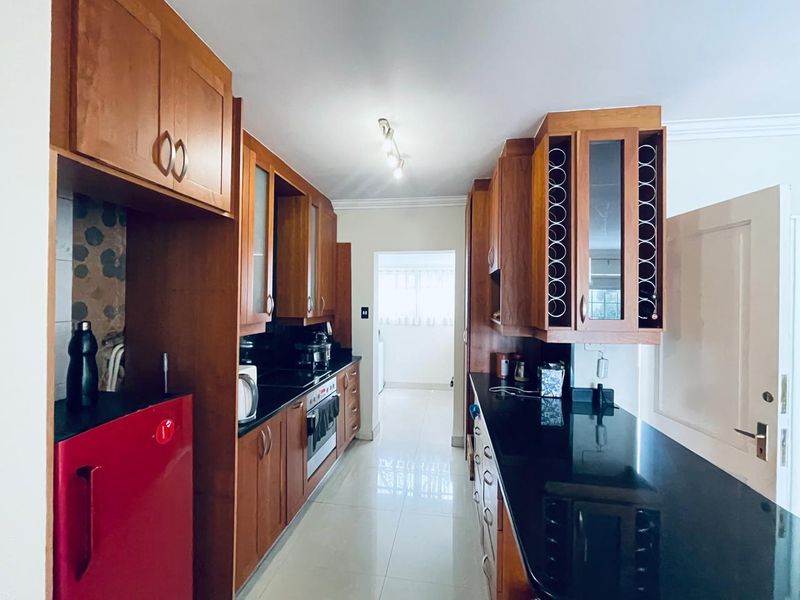 A galley-style kitchen featuring warm-toned wooden cabinetry, contrasting black granite countertops, and tiled flooring, offering a functional and classic layout.