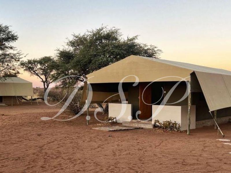 A view of a safari-style tented accommodation unit featuring a canvas structure and masonry entrance walls set in a dry, sandy landscape.