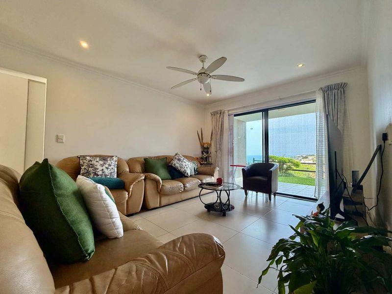 Spacious living room featuring tiled flooring, a ceiling fan, and large sliding glass doors that open to an outdoor area with scenic views.
