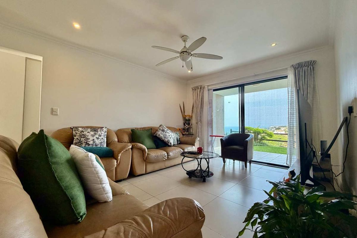 Spacious living room featuring tiled flooring, a ceiling fan, and large sliding glass doors that open to an outdoor area with scenic views.