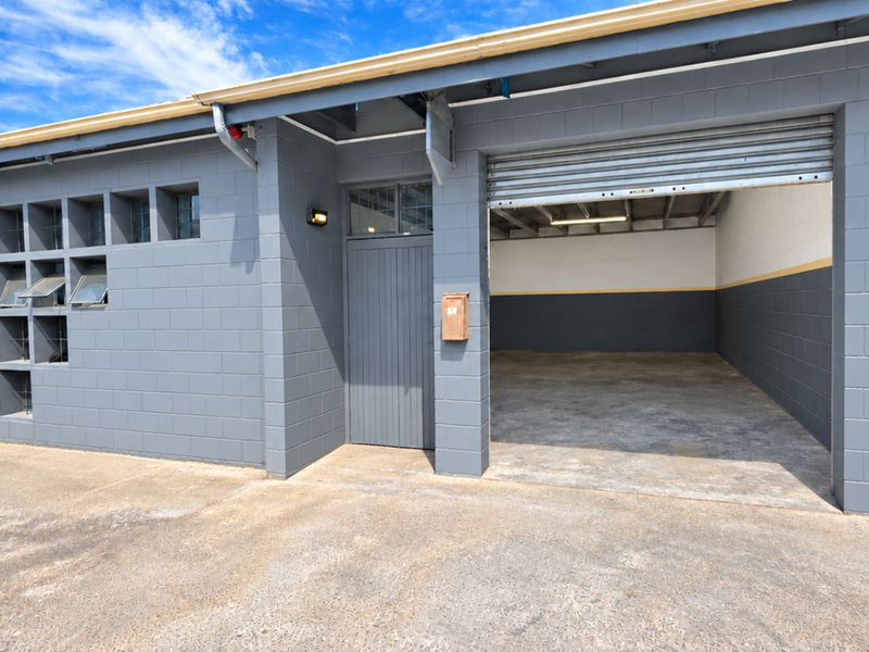 Industrial unit exterior featuring grey concrete block walls, a roller shutter door, a pedestrian entrance, and a concrete apron.