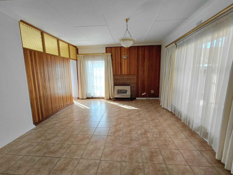Spacious living room featuring timber wall paneling, tiled flooring, and a built-in gas fireplace, offering a blank canvas for renovation.