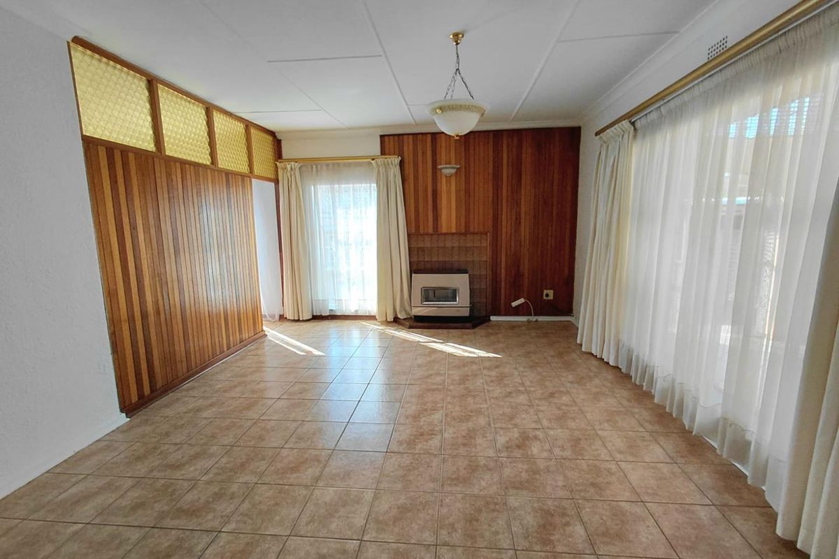 Spacious living room featuring timber wall paneling, tiled flooring, and a built-in gas fireplace, offering a blank canvas for renovation.