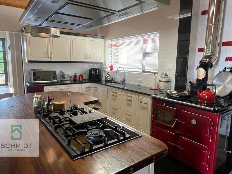 Spacious kitchen featuring a large wooden island with integrated gas hob, overhead extractor, and a classic red range cooker.