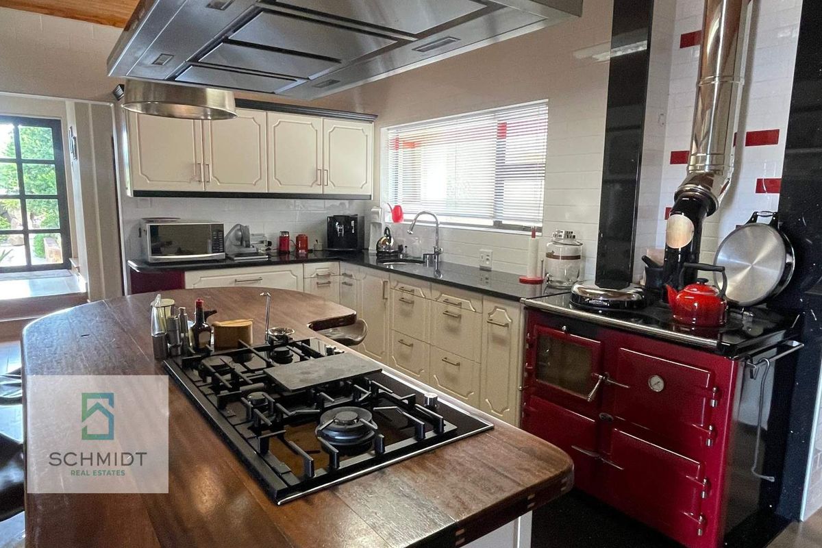Spacious kitchen featuring a large wooden island with integrated gas hob, overhead extractor, and a classic red range cooker.
