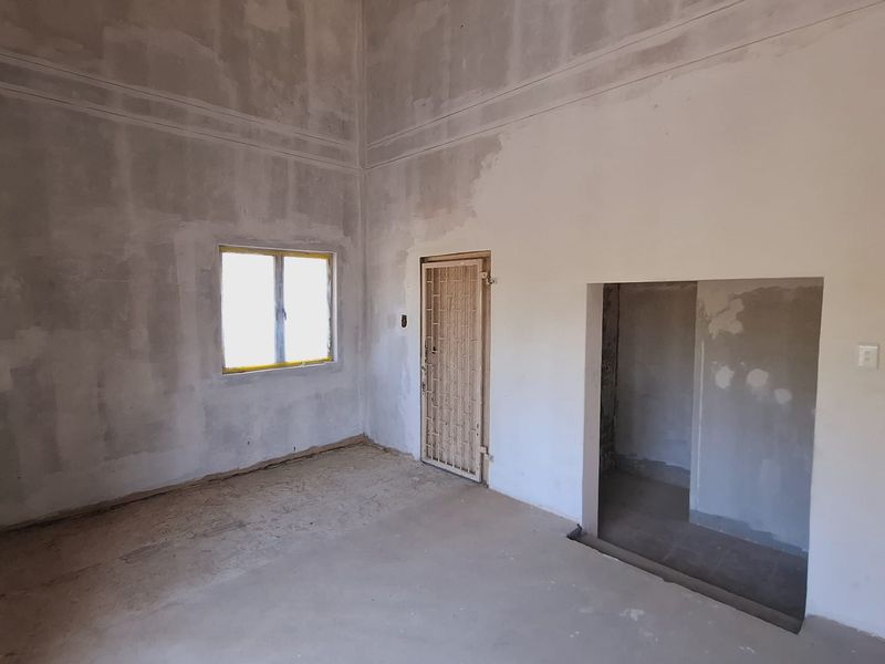 An unfinished interior space featuring high ceilings, exposed concrete flooring, and raw plaster walls, offering a blank canvas for renovation.