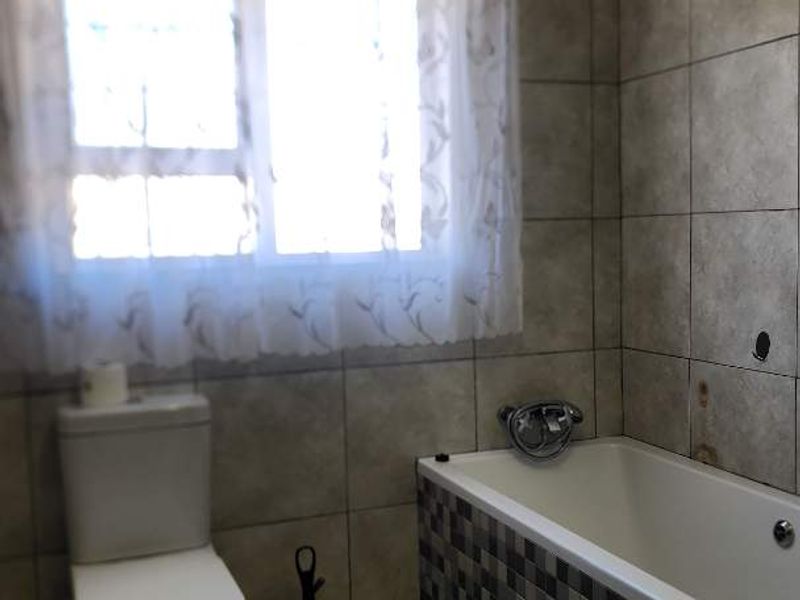 A functional bathroom featuring a bathtub with a mosaic-tiled surround, a standard toilet, and neutral wall tiling.