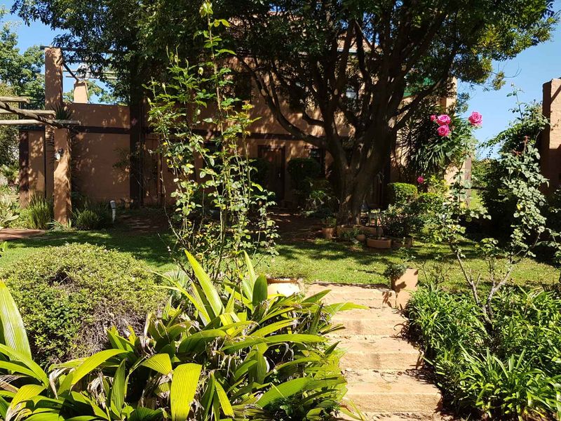 A view of the rear garden featuring mature trees, established landscaping, and stone steps leading toward the building facade.