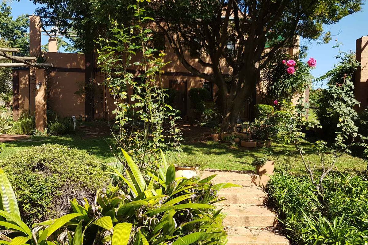 A view of the rear garden featuring mature trees, established landscaping, and stone steps leading toward the building facade.