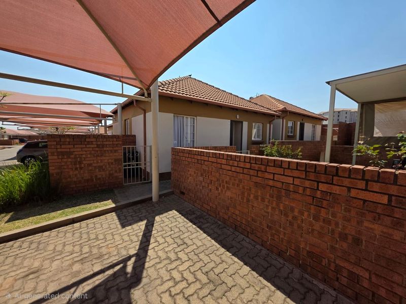 Front exterior view of a townhouse featuring a paved driveway, brick boundary wall, and a shade cloth carport structure.