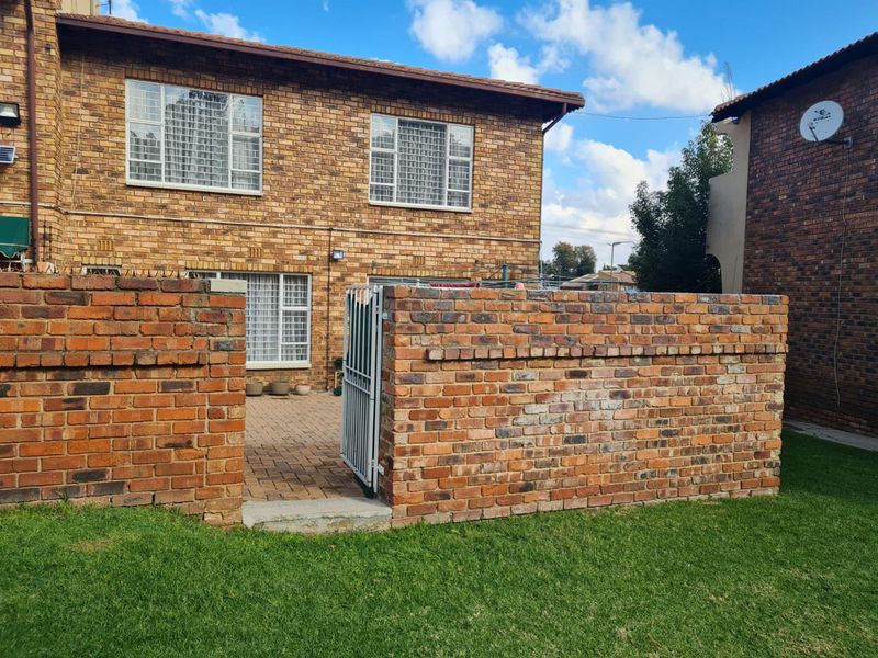 Rear view of a face-brick cluster home featuring a private paved patio area enclosed by a brick boundary wall and security gate.