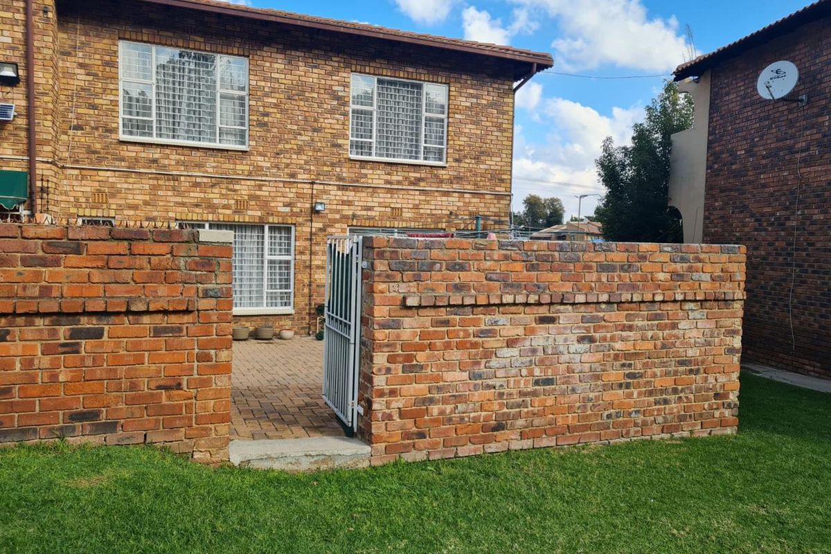 Rear view of a face-brick cluster home featuring a private paved patio area enclosed by a brick boundary wall and security gate.