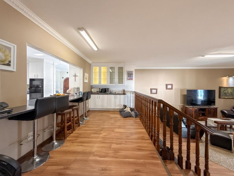 Open plan living area featuring laminate flooring, a wooden balustrade, and a built-in breakfast bar with adjacent cabinetry.