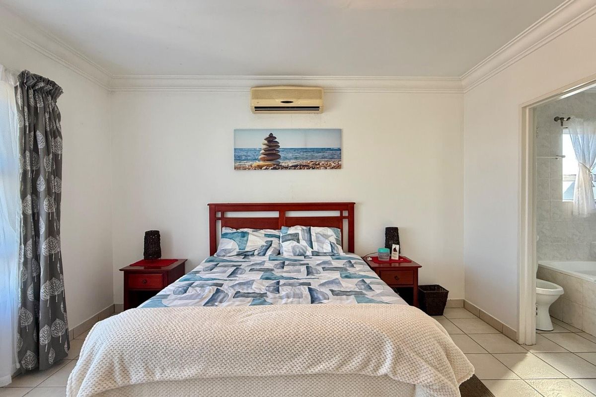A well-lit bedroom featuring tiled flooring, crown molding, and an en-suite bathroom, equipped with a wall-mounted air conditioning unit.