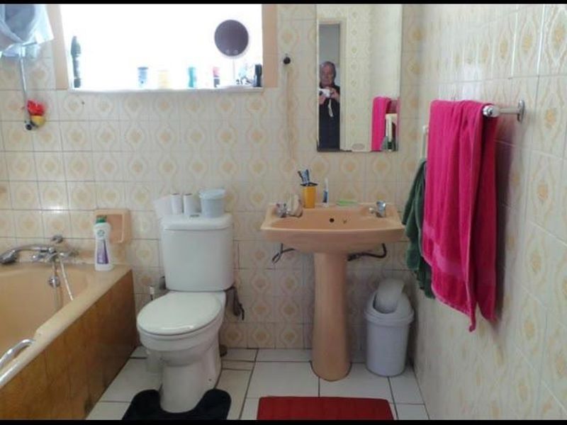 A dated bathroom featuring a pedestal basin, bathtub, and toilet with original wall tiling throughout.