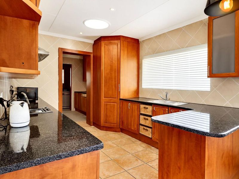 A well-maintained kitchen featuring warm wooden cabinetry, dark granite countertops, a functional layout, and a skylight providing natural light.