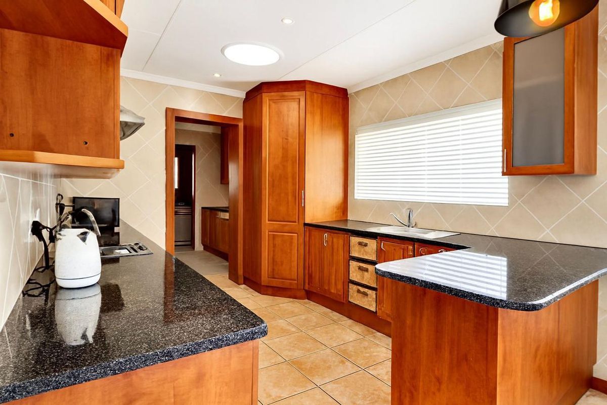 A well-maintained kitchen featuring warm wooden cabinetry, dark granite countertops, a functional layout, and a skylight providing natural light.