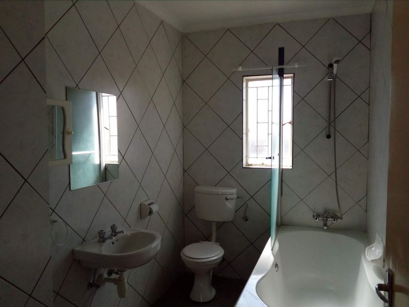 A functional bathroom featuring a bathtub with a shower mixer, a wall-mounted basin, and a toilet, finished with diamond-patterned wall tiles.